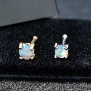 May include: Two nose rings with opal stones, one with a gold setting and one with a silver setting, displayed in a black velvet box.