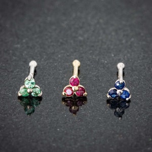 Könnte beinhalten: Drei Nasenringe mit verschiedenen farbigen Edelsteinen. Die Ringe sind aus Gold und haben jeweils drei Edelsteine. Die Edelsteine sind grün, rot und blau.