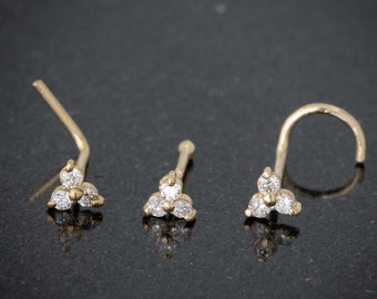 May include: Three gold nose rings with a cluster of three small diamonds each. The rings are on a black surface.
