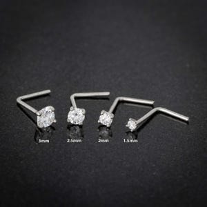 May include: Five silver nose rings with clear cubic zirconia stones. The stones are 1.5mm, 2mm, 2.5mm, and 3mm in diameter.