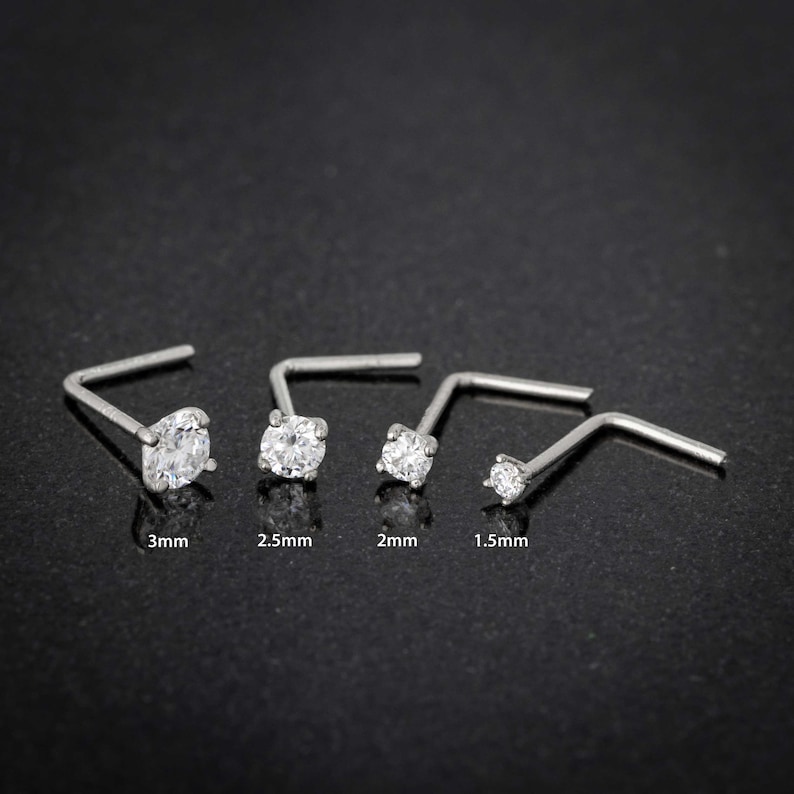 May include: Five silver nose rings with clear cubic zirconia stones. The stones are 1.5mm, 2mm, 2.5mm, and 3mm in diameter.