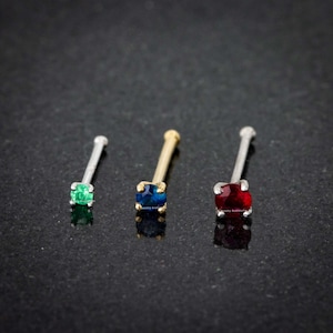 May include: Three nose rings with different colored gemstones. The rings are made of silver and gold. The gemstones are green, blue, and red.