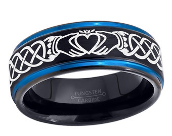 Könnte beinhalten: Ein schwarzer Ring aus Wolframkarbid mit blauem Innenband und blauer abgeschrägter Kante. Die Außenfläche zeigt ein weißes, lasergraviertes Claddagh-Motiv mit Händen, die ein Herz halten, und ein durchgehendes keltisches Knotenmuster. Innen ist TUNGSTEN CARBIDE eingraviert.