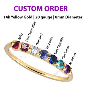May include: A custom order ring made of 14k yellow gold with a 20 gauge band and an 8mm diameter. The ring features a series of gemstones including ruby, pink tourmaline, diamond, tanzanite, blue sapphire, blue topaz, and amethyst.