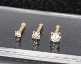 May include: Three gold nose rings with clear round gemstones. The rings are different sizes.