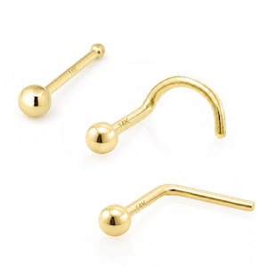 May include: Three 14K gold nose studs with polished spherical ends. One stud is straight, one features a curved hook shape, and one has an L-shaped post. Each piece is stamped with 14K text on the post, showcasing a smooth, reflective metallic finish.