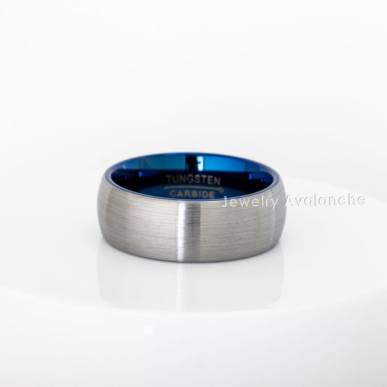 Peut inclure: Une bague en carbure de tungst&egrave;ne argent&eacute; avec une finition bross&eacute;e et un int&eacute;rieur bleu vif. La bague porte l'inscription "Tungsten Carbide" &agrave; l'int&eacute;rieur. Jewelry Avalanche est imprim&eacute; sur le c&ocirc;t&eacute;.