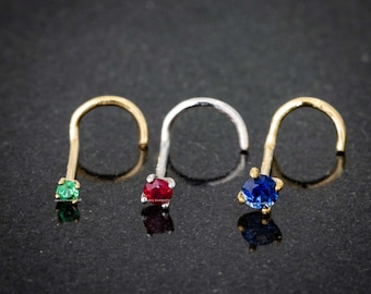 Könnte beinhalten: Drei Nasenringe mit verschiedenen Edelsteinen. Die Ringe sind aus Gold und Silber. Die Edelsteine sind grün, rot und blau.