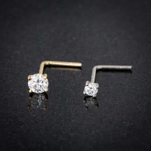 May include: Two nose rings with clear round gemstones. The nose ring on the left is gold and the nose ring on the right is silver.