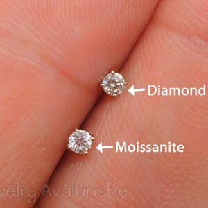 May include: Close-up of two small round gemstones set in metal. The gemstone on the left is labeled "Moissanite" and the gemstone on the right is labeled "Diamond".