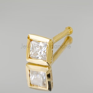 May include: Gold nose ring with a square-shaped clear gemstone.