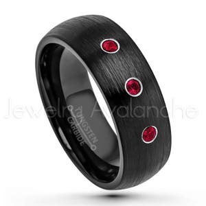 May include: A black tungsten carbide ring with a brushed finish featuring three round, bezel-set red stones arranged in a vertical line. The interior of the band is engraved with the text Tungsten Carbide and Jewelry Avalanche.
