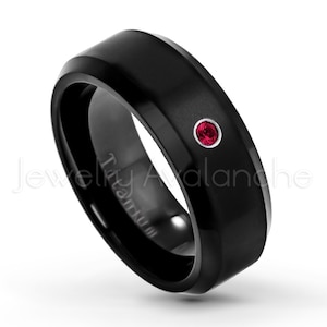 May include: Black titanium ring with a single red gemstone set in the center. The ring is engraved with the word "Titanium".