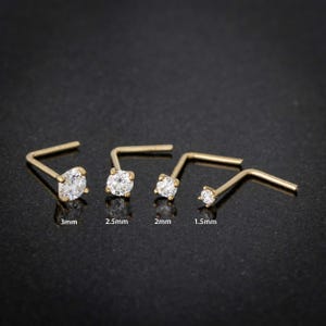 May include: Four gold nose rings with clear cubic zirconia stones. The stones are 3mm, 2.5mm, 2mm, and 1.5mm in size.