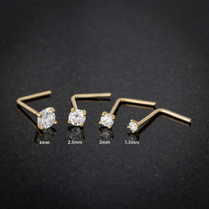 May include: Four gold nose rings with clear cubic zirconia stones. The stones are 3mm, 2.5mm, 2mm, and 1.5mm in size.