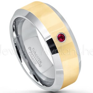 May include: A two-tone tungsten carbide ring with a silver-colored band and a gold-colored center. A small, round, red gemstone is set into the gold band. The ring is labeled "Tungsten Carbide".