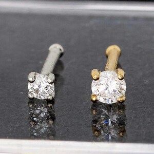 May include: Two nose rings with clear cubic zirconia stones. The nose ring on the left has a silver post and the nose ring on the right has a gold post.