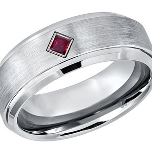 May include: A brushed silver wedding band with a single, square-shaped ruby gemstone set in the center.