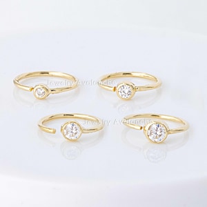 May include: Four gold hoop earrings with a single clear gemstone set in each hoop. The hoops are open and have a hinged closure.
