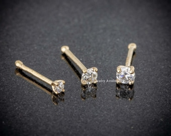 May include: Three gold nose rings with clear gemstones. The rings are different sizes.