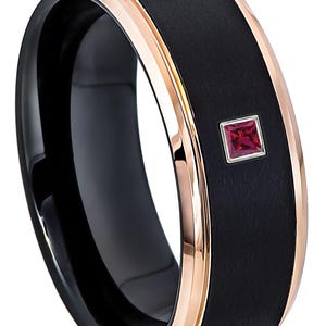 May include: A black tungsten carbide ring with a rose gold band and a small red gemstone. The ring has a brushed finish.
