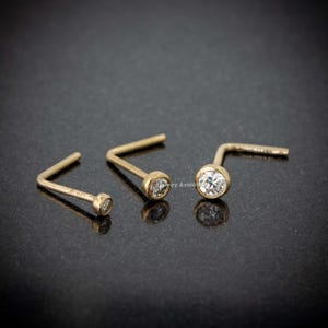 May include: Three gold nose rings with clear round gemstones. The rings are L-shaped and have a polished finish.