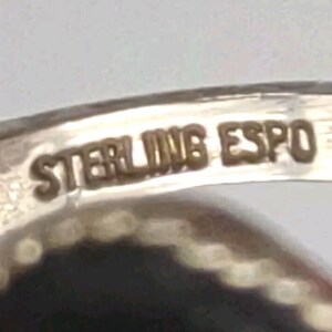May include: Close-up of a silver ring with the inscription "STERLING ESPO" on the inside band.