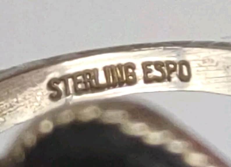 May include: Close-up of a silver ring with the inscription "STERLING ESPO" on the inside band.