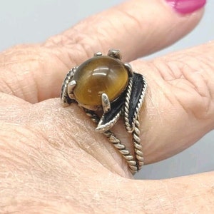 May include: A silver ring with a brown tiger's eye stone set in a leaf design. The ring is on a finger.