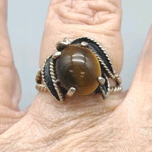 May include: A silver ring with a large, round, brown tiger's eye stone set in a twisted, leaf-shaped design.