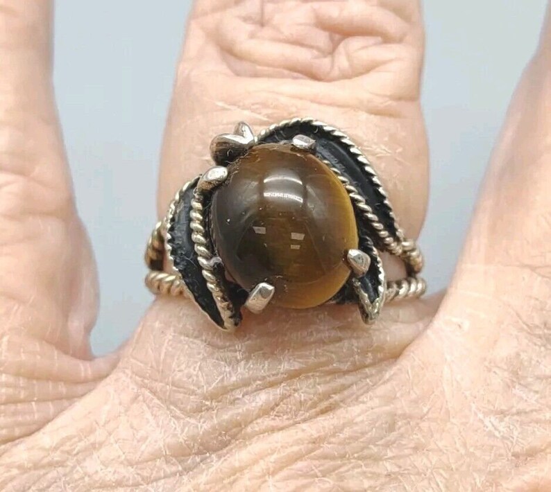 May include: A silver ring with a large, round, brown tiger's eye stone set in a twisted, leaf-shaped design.
