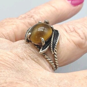 May include: A silver ring with a brown tiger's eye stone set in a leaf design. The ring is on a finger.