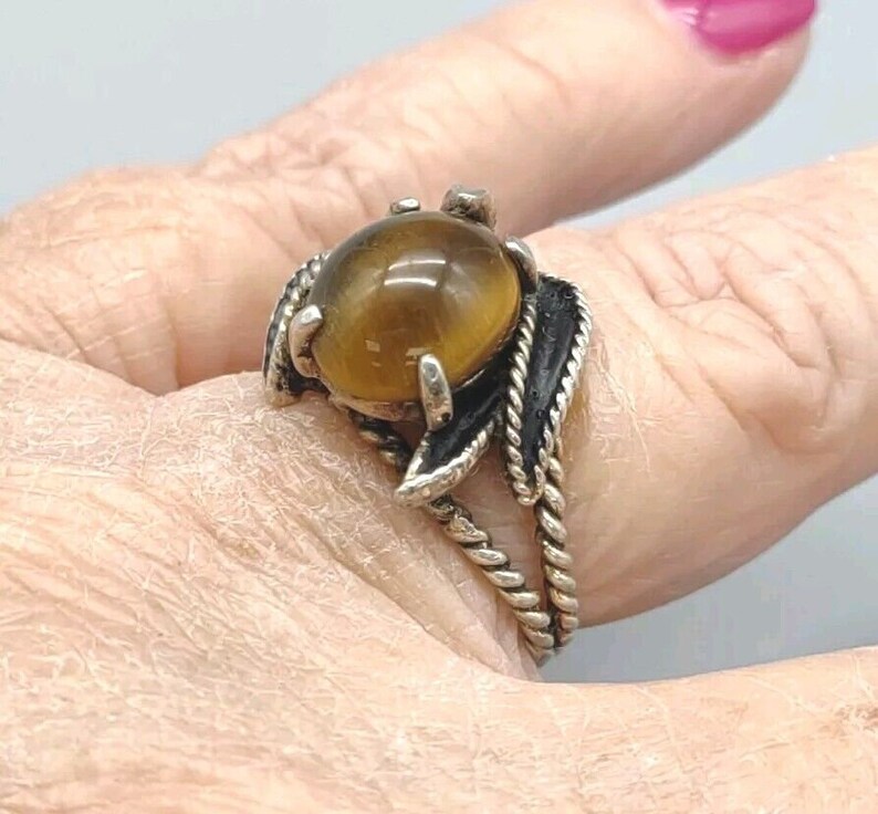 May include: A silver ring with a brown tiger's eye stone set in a leaf design. The ring is on a finger.