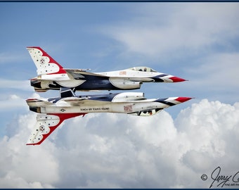 Puede incluir: Dos aviones de combate F-16 vuelan en formación, uno encima del otro, contra un cielo azul con nubes blancas. Los aviones están pintados con los colores de la bandera de los Estados Unidos, con rayas rojas, blancas y azules y estrellas.