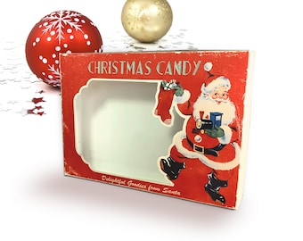 Peut inclure: Une boîte de bonbons de Noël rouge et blanche avec une fenêtre montrant le Père Noël tenant une chaussette et une tasse. La boîte porte le texte "Christmas Candy" et "Delightful Goodies from Santa".