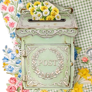 May include: A vintage-style, mint green metal mailbox with a distressed finish. The mailbox features a floral wreath design around the word "POST" and is adorned with decorative trim. A bouquet of yellow and white daisies sits atop the mailbox.