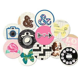 May include: A selection of circular paper cutouts with diverse designs. Features a camera, an ampersand, a floral pattern, an arrow with a heart, a crossword, a puppy, and a rotary phone. The cutouts are in various colours.