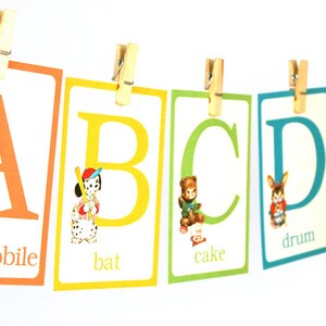 May include: A colorful alphabet chart with illustrations and words for each letter. The letters are A, B, C, D, and E. The words are automobile, bat, cake, drum, and eggs.