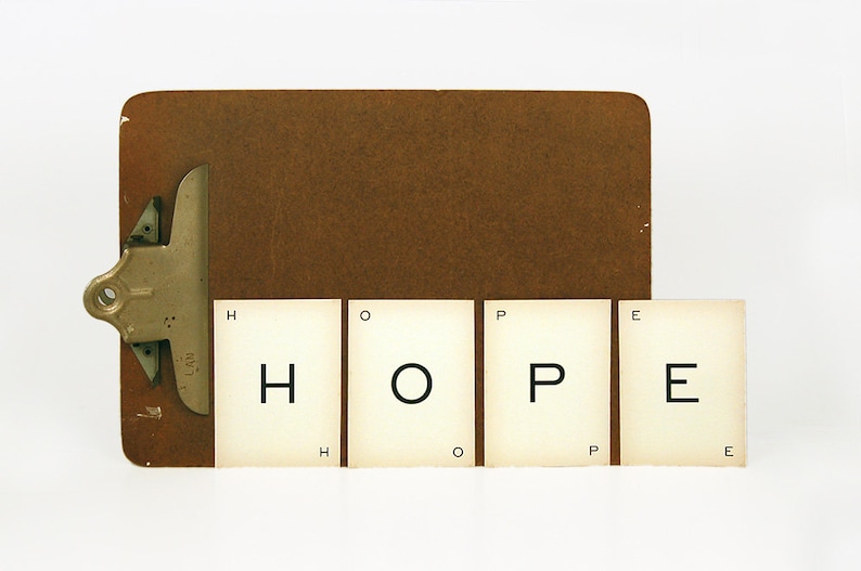 May include: A brown clipboard with a metal clip holds four white cards with the word "HOPE" spelled out in black letters.