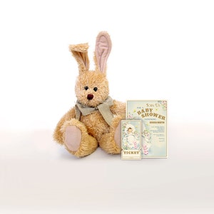 Puede incluir: Un juguete de peluche de conejo marr&oacute;n con una bufanda gris se sienta junto a una invitaci&oacute;n a una fiesta de bienvenida al beb&eacute; con el texto "Join Us For A Baby Shower Honoring Jessica Martin".