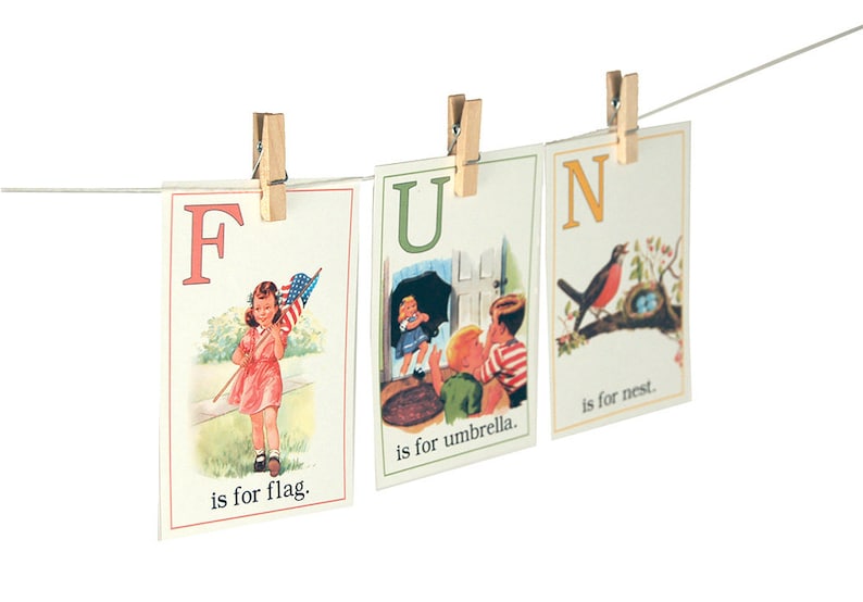 May include: Three alphabet flashcards with a clothespin on each. The first card shows the letter F and a girl holding a flag. The text reads "F is for flag." The second card shows the letter U and a girl holding an umbrella. The text reads "U is for umbrella." The third card shows the letter N and a bird sitting on a nest. The text reads "N is for nest."