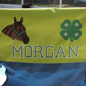 Puede incluir: Una silla verde y negra con un respaldo de tela verde. El respaldo tiene un caballo bordado, un tr&eacute;bol 4-H y el nombre "MORGAN".