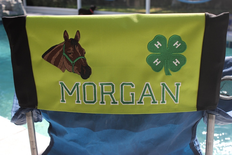 Puede incluir: Una silla verde y negra con un respaldo de tela verde. El respaldo tiene un caballo bordado, un tr&eacute;bol 4-H y el nombre "MORGAN".