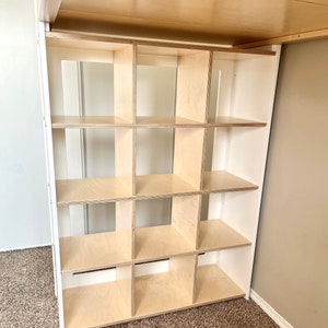 May include: A white shelf unit with 12 square compartments. The shelves are made of light wood and are empty.