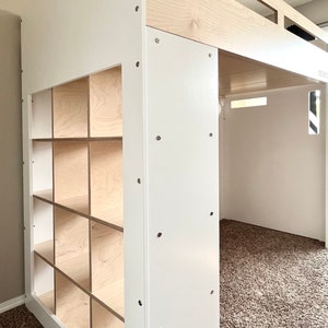 May include: White loft bed with a built-in bookshelf. The bed has a white frame and a natural wood top. The bookshelf has 9 cubbies.