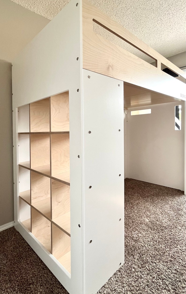 May include: White loft bed with a built-in bookshelf. The bed has a white frame and a natural wood top. The bookshelf has 9 cubbies.