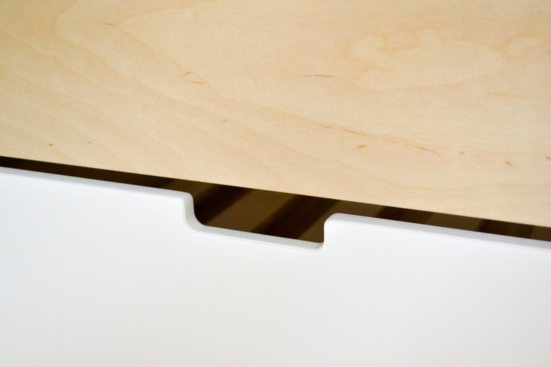 May include: A white drawer with a cutout handle. The drawer is made of wood and has a light wood top.