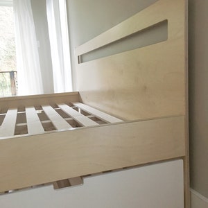 May include: A light wood platform bed frame with a white drawer underneath. The headboard has a rectangular cutout.