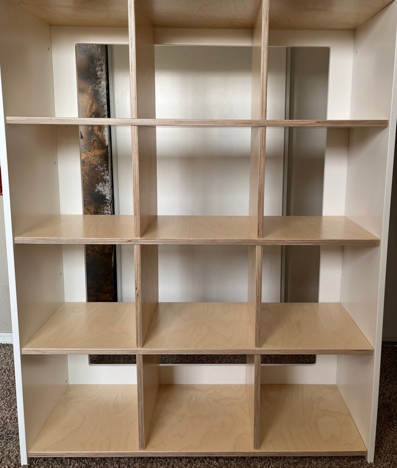 May include: White cube shelf unit with 12 compartments. The shelves are made of light wood and the frame is white.