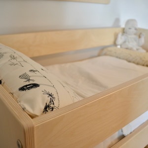 May include: A wooden crib with a white sheet and a patterned pillow. A stuffed toy sits on the crib mattress.